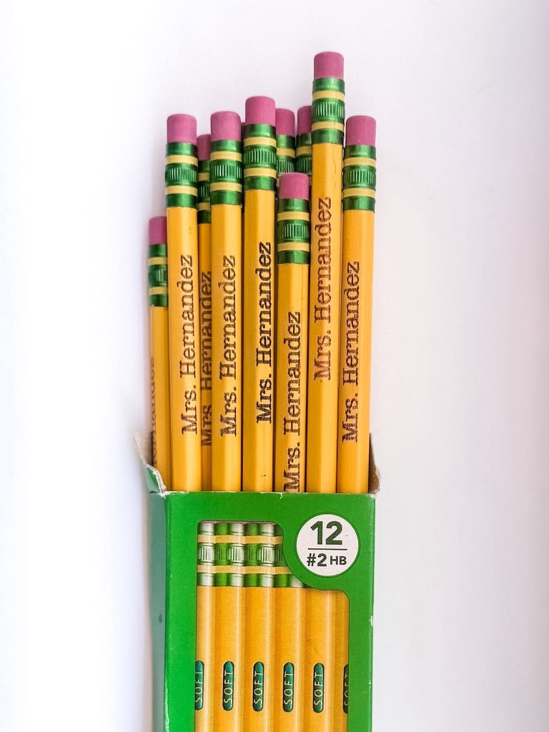 A green cardboard pencil box containing 12 #2 HB Soft Pencils with green and yellow striped eraser ends engraved with the name "Mrs. Hernandez" near the eraser end.